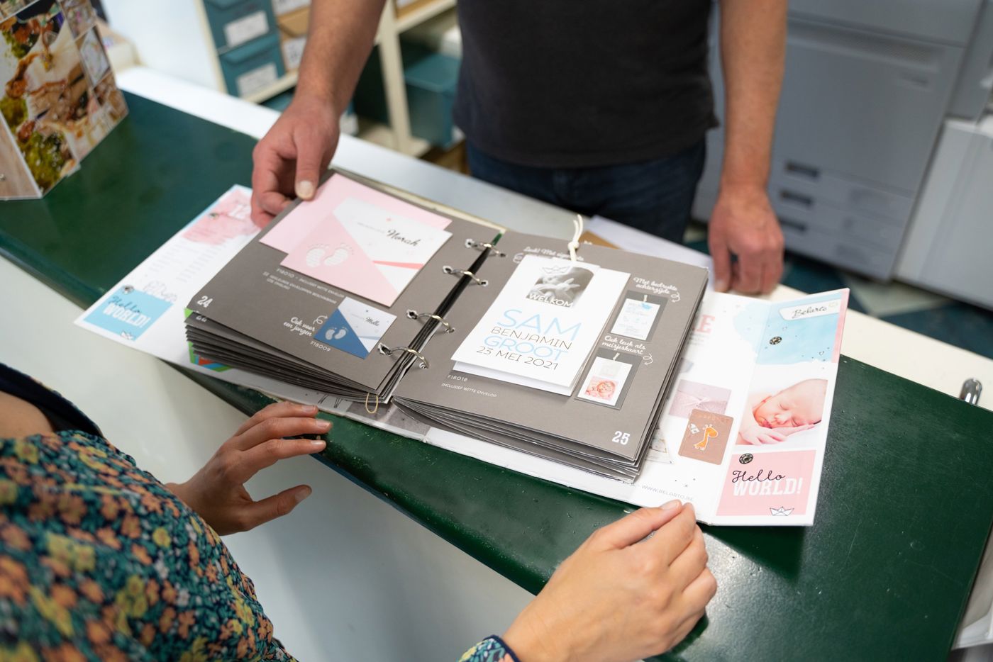 Klant achter balie in Drukkerij Zaansprint die door inspiratie boeken aan het bladeren is Klant achter balie in Drukkerij Zaansprint die door inspiratie boeken aan het bladeren is